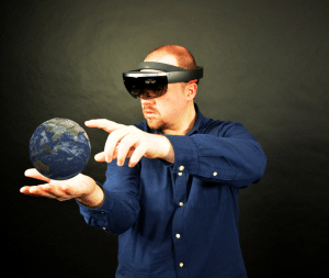 Bild eines Menschen, der eine Microsoft HoloLens trägt und ein 3D Modell der Erde auf seiner Hand bearbeitet.